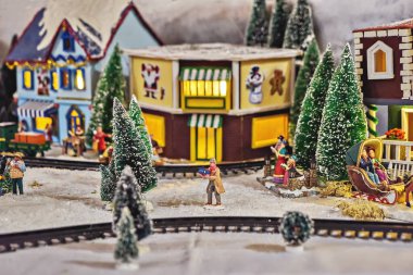 Miniature colored houses and figures of people during celebration of Christmas, snowy streets, and glowing lanterns. Miniature toy city during winter season. City scene in miniature models
