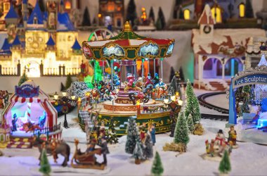 Cheerful miniature carousel with toy people in winter park during Christmas market. Miniature toy city during the winter season. City scene in miniature models clipart