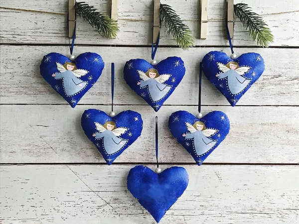 Six big hearts with angels pinned on wall with pine branches. Handmade baubles zero-waste Christmas