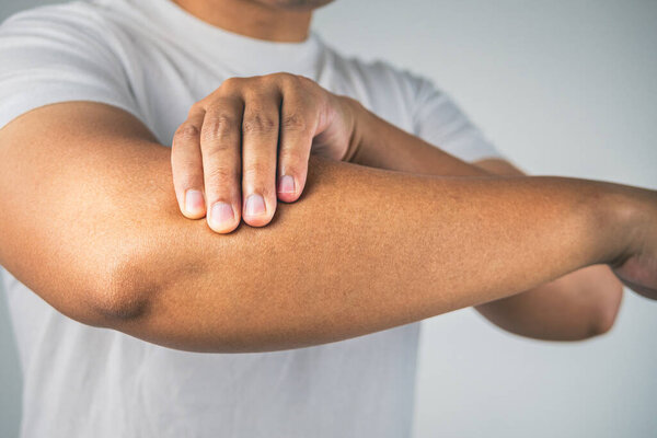 Tennis elbow concept. The man uses fingers to massage his arm. Healthcare knowledge. Medium close up shot.