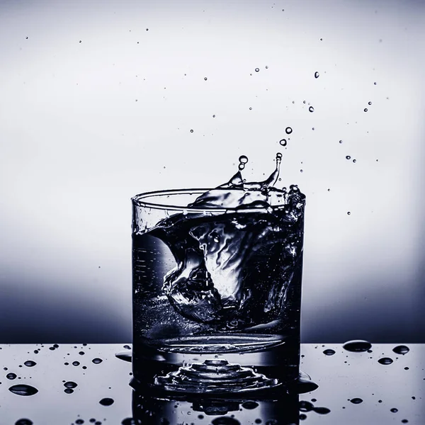 Fresh ice cube falling to glass of water splash isolated Stock Image