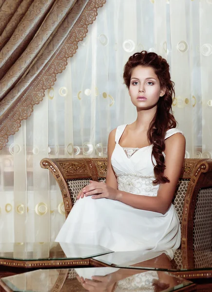 Vrouwelijkheid. bruin haar vrouw bruid in trouwjurk zitten. klassieke romantische interieur — Stockfoto