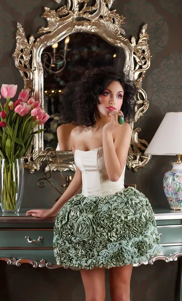 Кокетт. Женщина с вьющимися волосами в элегантном платье над винтажным зеркалом — стоковое фото