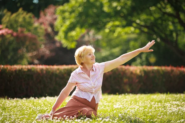 ध्यानधारणा करा. पार्क मध्ये कृत्रिम जुनी महिला तिचा हात ताणून — स्टॉक फोटो, इमेज
