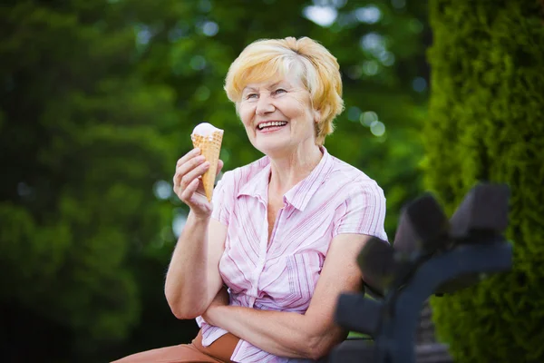 Mujer de pelo gris Relajándose con helado en el banco en el parque — Foto de Stock