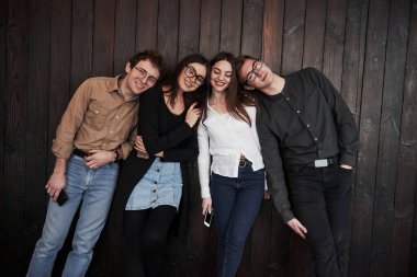 Rahatlamış ve mutlu. Gençlik siyah ahşap duvarın önünde duruyor. Bir grup arkadaş birlikte vakit geçiriyorlar..