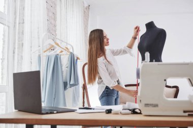 Mankenin boyunu ölçer. Kadın moda tasarımcısı atölyedeki yeni kıyafetler üzerinde çalışıyor..