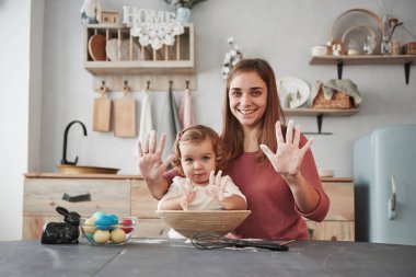 Çiçeklerle dolu elleri gösteriyor. Anne, kızına Paskalya tatili için yumurta boyamayı öğretiyor..
