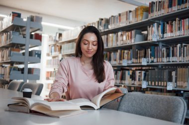 Sakin ve sessiz. Esmer kız kitaplarla dolu kütüphanede iyi vakit geçiriyor..