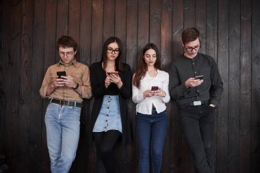 Sakin ve sakin. Gençlik siyah ahşap duvarın önünde duruyor. Bir grup arkadaş birlikte vakit geçiriyorlar..