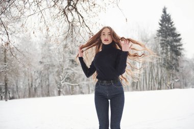 Saçlarla öne doğru koşmak farklı yönlere gider. Uzun saçlı ve siyah bluzlu güzel kız kış ormanında..