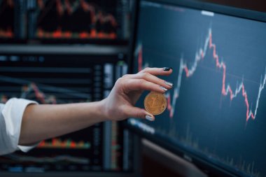 Manzarayı kapat. Modern ofiste birçok grafikli ekranı olan bir kadının eli Bitcoin 'i tutuyor.