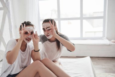 Her şey yolunda. Yüzünde beyaz maske kullanarak cilt bakımı kavramı. İki kız kardeş hafta sonunu yatak odasında geçirir..