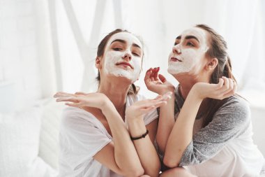 Halimize bak, harikayız. Yüzünde beyaz maske kullanarak cilt bakımı kavramı. İki kız kardeş hafta sonunu yatak odasında geçirir..