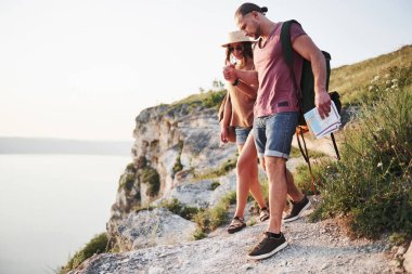 Sırt çantalı iki turist dağın tepesine tırmanıyor ve güneşin doğuşunun tadını çıkarıyor..