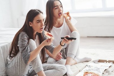 Filmi izleyemiyorum. Gündüz vakti güzel yatak odasının zemininde oturan kız kardeşler televizyon izlerken pizza yiyorlar..