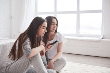 Kız kardeşler gündüz vakti güzel yatak odasının zemininde otururken televizyon izlerken eğleniyorlar..