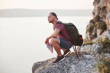 Haritası olan çekici bir adam su yüzeyinin üstündeki dağların manzarasının tadını çıkarıyor. Seyahat yaşam tarzı macera tatili konsepti.