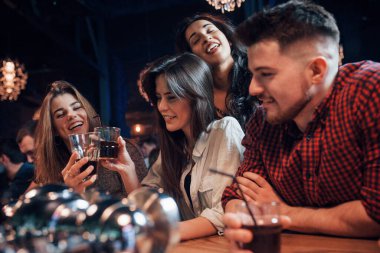 Viski iç. Gece kulübünde gülümseyen ve kadeh kaldıran bir grup genç arkadaş..