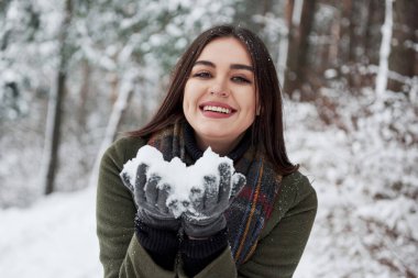 Ellerinde kar tutan ve gülümseyen mutlu esmer. Kış Ormanı.