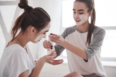 Yüzünde beyaz maske kullanarak cilt bakımı kavramı. İki kız kardeş hafta sonunu yatak odasında geçirir..