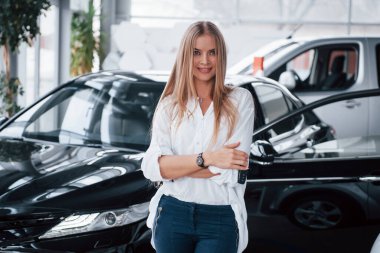 Kollarını kavuşturarak. Tamirhanedeki genç müdür mükemmel cilalanmış siyah arabaya karşı duruyor..