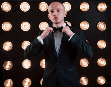 Kravatını düzeltir. Gösteri için hazırız. Siyah takım elbiseli sihirbaz sahne arkasında özel ışıklandırmayla odada duruyor..