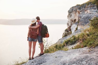 Sırt çantalı iki erkek ve kadın turist dağın tepesinde durup güneşin doğuşunun tadını çıkarıyorlar. Seyahat yaşam tarzı macera tatili konsepti.
