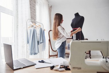 Kuklanın genişliğini ölçme işlemi. Kadın moda tasarımcısı atölyedeki yeni kıyafetler üzerinde çalışıyor..