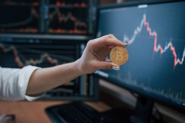 Fikir alışverişi. Modern ofiste birçok grafikli ekranı olan bir kadının eli Bitcoin 'i tutuyor.