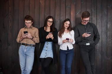 Herkes akıllı telefonuna bağımlıydı. Gençlik siyah ahşap duvarın önünde duruyor. Bir grup arkadaş birlikte vakit geçiriyorlar..