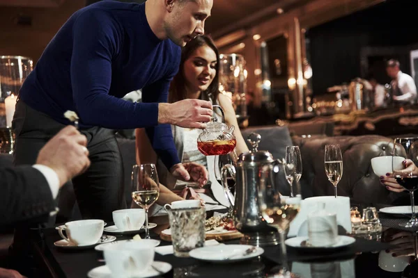 穿着蓝色衬衫的男人拿着新鲜的茶 家人朋友们在漂亮的豪华现代餐厅玩得很开心 — 图库照片