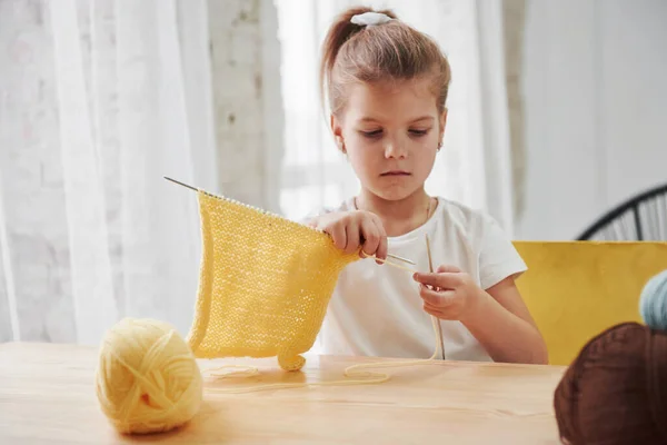 彼女はそれが得意だ 子供は家で編んでいる かわいい女の子は木のテーブルの近くに座っているいくつかの新しいものを学んでいる — ストック写真