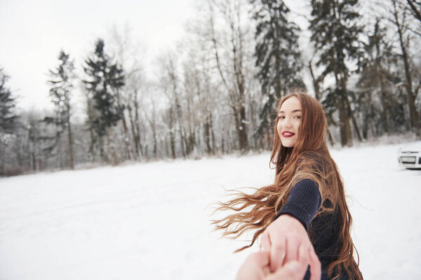 Hurry up please. Girl with long hair goes near the forest to the automobile in wintertime.