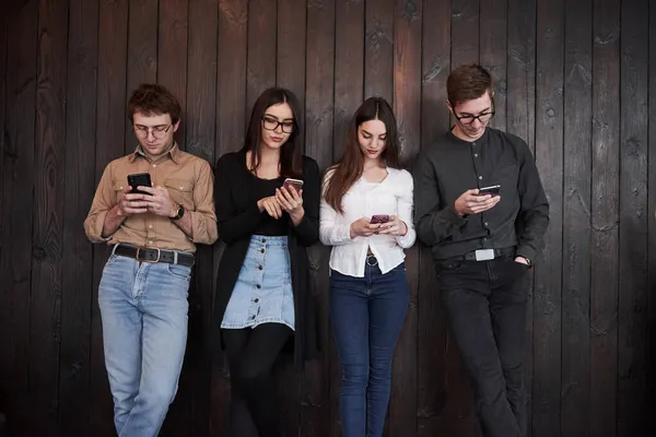 Stirrar Telefonerna Ungdom Står Mot Svart Trävägg Grupp Vänner Som — Stockfoto