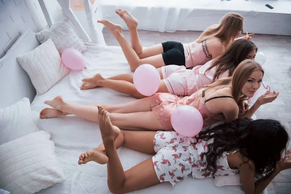 拿杯喝的躺在豪华的白色床上的年轻姑娘们都在庆祝 侧视图和顶部视图 — 图库照片