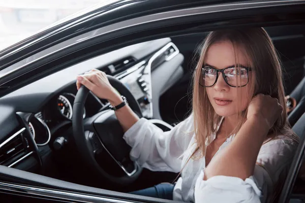 Okularach Piękna Blondynka Siedzi Nowym Samochodzie Nowoczesnym Czarnym Wnętrzem — Zdjęcie stockowe