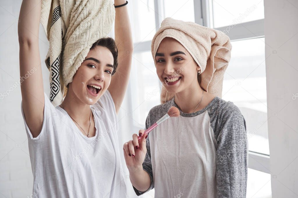 Playing around. Sisters have skincare using brush with powder. With towels on the heads.