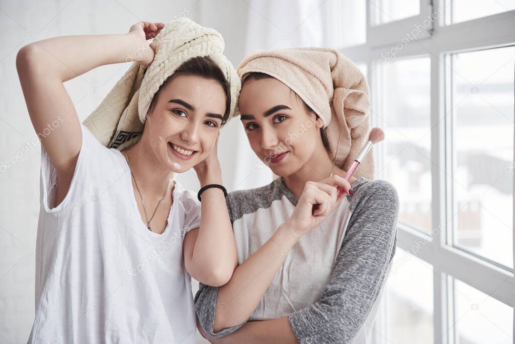 Posing for the camera. Sisters have skincare using brush with powder. With towels on the heads.