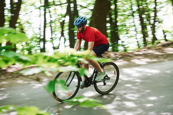 侧视图 骑自行车的人在森林里的柏油路上 — 图库照片