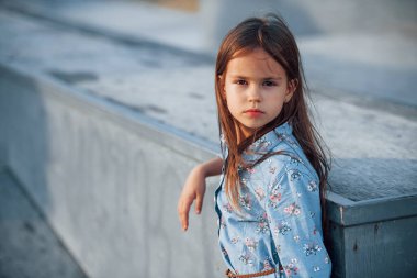 Mavili küçük kız, rampaya yaslandığında şehirde bir kameraya poz veriyor..