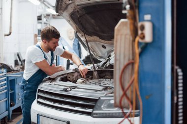 Yeni parçalar yerleştiriyorum. Mavi üniformalı işçi otomobil salonunda çalışıyor..