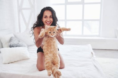 Ne uzun bir kedi. Çekici sarışın beyaz yatakta tatlı kedisiyle dinleniyor..