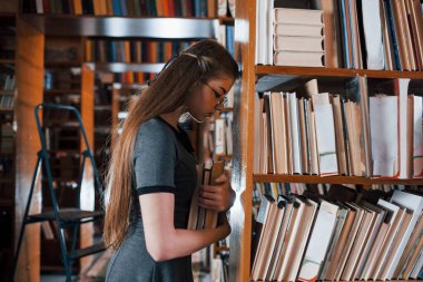 Raflara yaslanarak. Yorgun hissediyorum. Kütüphanede kitaplarla dolu bir kız öğrenci var. Eğitim kavramı.