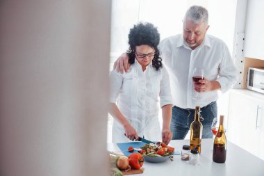 Tatilleri kutluyoruz. Beyaz gömlekli adam ve karısı mutfakta sebze kullanarak yemek hazırlıyorlar..