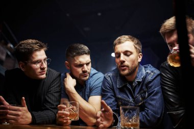 Ön manzara. Arkadaşlar ellerinde alkolle barda dinleniyorlar. Sohbet ederken.