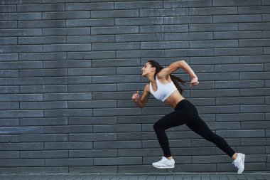 Hızlı koşuyor. Genç, sportif esmer, ince vücutlu, şehirde gündüz vakti tuğla duvara yaslanmış..