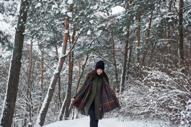 Sıcak giysili neşeli genç kız gündüz vakti kış ormanında yürüyüşe çıkıyor..
