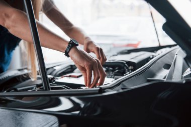Odaklan. Güzel bir iş için. Araba bağımlısı kadın siyah otomobili kapalı alanda tamir ediyor..