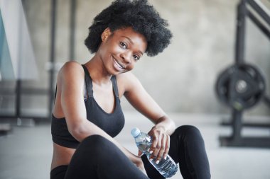 Dost canlısı bir bayan mola veriyor. Kıvırcık saçlı ve spor elbiseli Afrikalı Amerikalı kadın spor salonunda spor yapıyor..